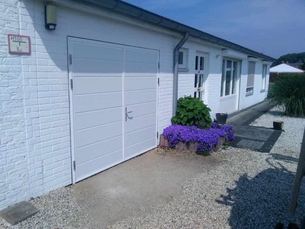 Stijlvolle dubbele witte garagepoorten voor uw huis in Sittard- Geleen of Limburg. Moderne witte dubbele garagepoorten, passend bij een lichte woning met bloemen voor de deur.